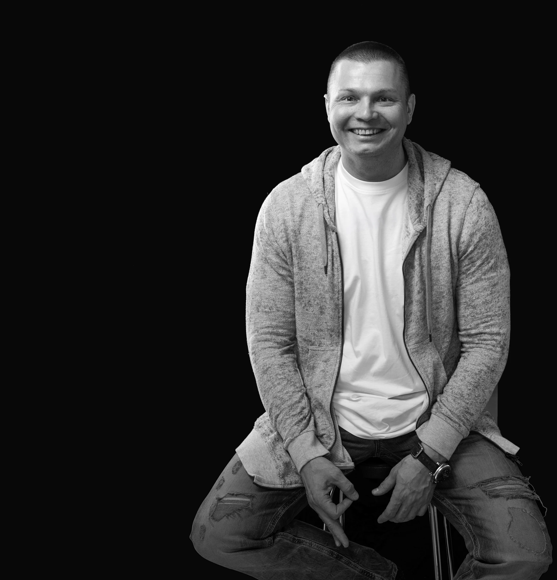 Otto Tuomainen istuu ja hymyilee tummalla taustalla